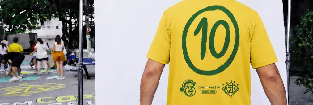 Costas da camisa 10 amarela CazéTV com número 10 verde, usada na rua em dia de jogo